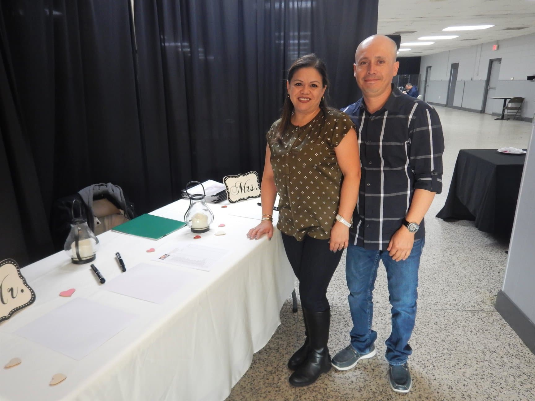 Smiling couple standing beside a table decorated with lanterns and 'Mr.' and 'Mrs.' signs.